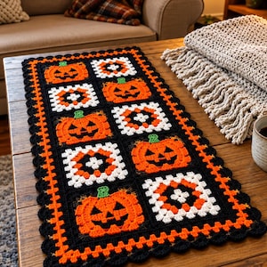 Puede incluir: Un camino de mesa rectangular de ganchillo con un patrón repetitivo de calabazas de Halloween naranjas con tallos verdes y cuadrados de la abuela en blanco, naranja y negro. El camino tiene un borde festoneado negro con una fila naranja.