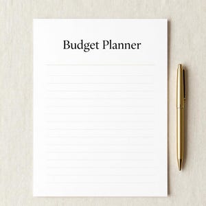 Può includere: Un foglio di carta bianco a righe con la scritta "Budget Planner" in nero. Una penna dorata è appoggiata a destra. Lo sfondo è di colore beige neutro.