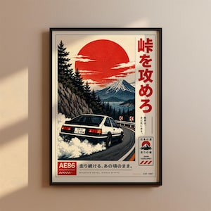 Op de afbeelding: Een ingelijste poster met een witte en zwarte AE86-auto die drift op een bergweg met een grote rode zon, de berg Fuji en dennenbomen op de achtergrond. De tekst bevat Japanse karakters, AE86 en de zin Mountain Roads, Higher Spirits.