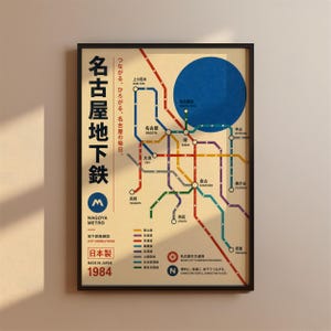 May include: A framed poster featuring a stylised map of the Nagoya Metro system with colourful transit lines, Japanese and English text, a large blue circle, and the year 1984. The design includes a legend for the lines and station names.