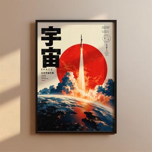 以下が含まれることがあります： 大きな赤い円を背景に宇宙へ打ち上げられるロケットが描かれた額入りポスター。デザインには宇宙を表す日本語の漢字、Space、Japan Space Program、Tanegashima Launch Siteというテキストと座標が含まれています。