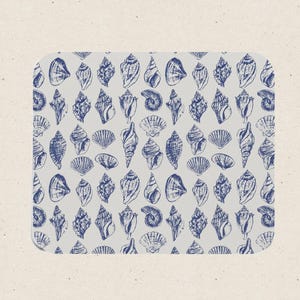 May include: A rectangular mat featuring a repeating pattern of dark blue line-drawn seashells on a light gray background. The various shell shapes include spiral, conch, and fan-like designs arranged in a grid-like layout across the surface.