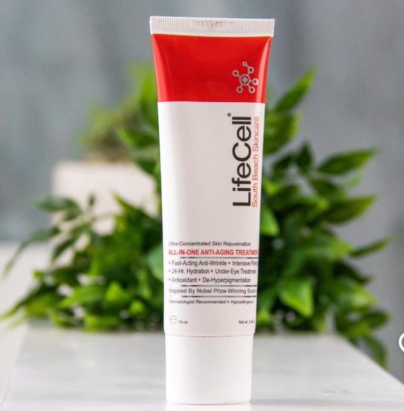 May include: A white and red tube of LifeCell South Beach Skincare anti-aging treatment. The tube features the brand name and product information, including "ALL-IN-ONE ANTI-AGING TREATMENT." The background includes green foliage.