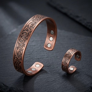 May include: A copper-toned metal cuff bracelet and a matching open ring, both featuring an intricate embossed Celtic knotwork pattern. The interior of each piece is fitted with small, circular silver-colored magnets at the open ends.