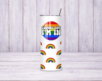 May include: White tumbler with a rainbow design and the text "SOUNDS GAY I'M IN". The tumbler also features repeating rainbow graphics. A silver straw is inserted in the lid.