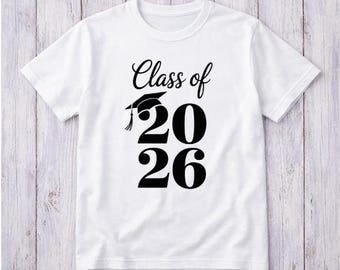May include: White t-shirt with the text "Class of 2026" in black, featuring a graduation cap graphic. The design is centered on the front of the shirt. The shirt is made of a soft material.