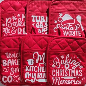 May include: A set of six red quilted oven mitts with pockets, each featuring white graphic text and holiday-themed icons including a Santa hat, a spoon, a rolling pin, and snowflakes. The designs include phrases like Baking Christmas Memories.