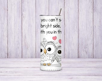 May include: A white cylindrical tumbler with a metal straw featuring a black line art illustration of two owls perched on a branch. Above the owls are two pink hearts and the text: If you can't see the bright side, I will sit with you in the dark.