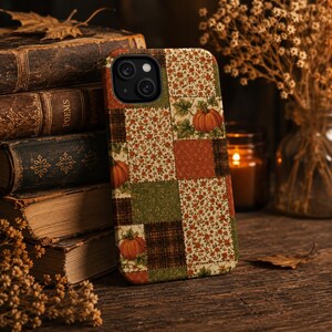 Puede incluir: Una funda rectangular para smartphone con un diseño de patchwork de varios cuadrados. El patrón incluye pequeños estampados florales naranjas, cuadros marrones oscuros, cuadrados de color naranja quemado y verde, con calabazas.