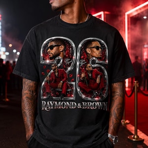 May include: A black short-sleeve t-shirt featuring a graphic print of two men in red suits, each framed within a large metallic number 2. The design includes the text "Usher Raymond," "Chris Brown," and "RAYMOND & BROWN" with red rose petals.