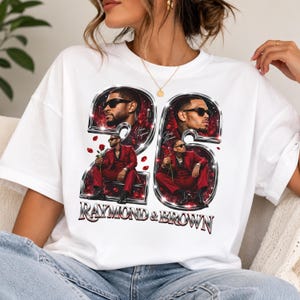 May include: A white t-shirt featuring a graphic print of the number 26 in a metallic chrome style. Inside the numbers are portraits of two men in red suits and sunglasses, with red rose petals scattered around. The text RAYMOND & BROWN is below.