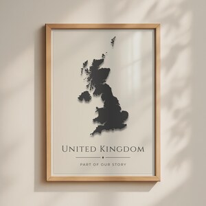May include: A framed wall art print featuring a black silhouette map of the United Kingdom centered on a light beige background. Below the map, the text reads UNITED KINGDOM followed by a horizontal line and the phrase PART OF OUR STORY.