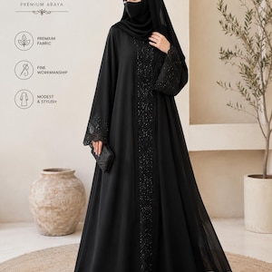 May include: A floor-length black abaya featuring a central vertical panel adorned with intricate black beadwork and sequins. The long sleeves have matching embellished cuffs. The garment is paired with a coordinating black hijab and face mask.