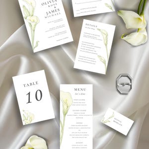 Puede incluir: Un conjunto de papelería de boda con tarjetas blancas, texto negro con serifa e ilustraciones de calas verdes. El set incluye una invitación, tarjeta de confirmación, tarjeta de detalles, número de mesa 10, menú y tarjeta de nombre, junto a un joyero plateado.