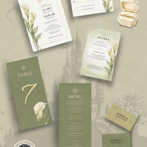 Könnte beinhalten: Ein Hochzeitspapeterie-Set bestehend aus einer weißen Einladung, Antwortkarte, Detailkarte, Tischnummer sieben, Menükarte und zwei Platzkarten in Salbeigrün und Weiß mit Calla-Lilien-Illustrationen, einem Kompass-Symbol und einer cremefarbenen Ringbox.