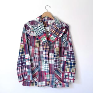 May include: A long-sleeve blazer featuring a patchwork design composed of various plaid and tartan fabric squares in shades of red, blue, yellow, green, and white. The garment includes a notched lapel, a button-front closure, and long sleeves.