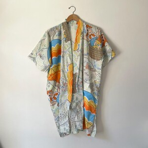 May include: A lightweight kimono-style robe featuring a colorful print of cartoon characters in baskets and hot air balloons. The fabric displays a repeating pattern of orange, blue, and green illustrations on a white background with short sleeves.