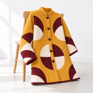 May include: A long-sleeved quilted coat in mustard yellow, featuring a repeating geometric pattern of large cream and deep maroon semicircles. The coat has a high collar, a front button closure with five dark buttons, and a diamond-stitched texture.