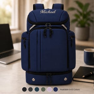 Può includere: Uno zaino blu navy con il nome Michael ricamato in corsivo bianco sullo scomparto superiore. La borsa include diverse sezioni con cerniera, tiretti neri e due dettagli circolari color argento sulla base inferiore.