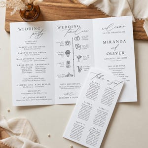 May include: A white tri-fold wedding programme and a matching rectangular seating chart card. The programme features black text detailing the wedding party, a timeline with icons, and the names Miranda and Oliver. The seating chart lists tables.