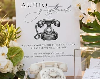 May include: A white sign with black text reading AUDIO guestbook and WE CAN'T COME TO THE PHONE RIGHT NOW, PLEASE LEAVE US A MESSAGE! A vintage-style rotary telephone sits in front of the sign next to a clear acrylic box containing white cards.
