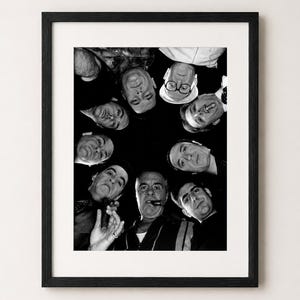Puede incluir: Impresión enmarcada en blanco y negro que presenta a un grupo de hombres mirando hacia abajo desde arriba. Los hombres están dispuestos en círculo, con sus rostros visibles. La impresión está en un marco negro y se muestra contra una pared blanca.