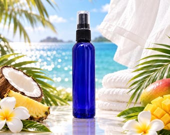 Pode incluir: Um frasco pulverizador cilíndrico de plástico azul cobalto com bocal de bomba preto. O frasco está posicionado na vertical, rodeado por um coco cortado ao meio, uma fatia de ananás, uma manga e duas flores de plumeria brancas.