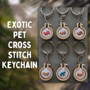 May include: Six circular wooden keychains featuring miniature cross-stitch designs of various exotic pets on white fabric. Each keychain includes a metal ring and chain attached to a small embroidery hoop frame. The text EXOTIC PET CROSS STITCH KEYCHAIN is visible on the left side.