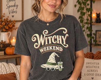 Könnte beinhalten: Ein anthrazitfarbenes Kurzarm-T-Shirt mit dem Text "WITCHY WEEKEND" in cremefarbener und roter Schrift. Unter dem Text befindet sich eine Grafik eines hellgrünen Hexenhutes, einer weißen Katzenaugen-Sonnenbrille und eines grünen Eiskaffeebechers.