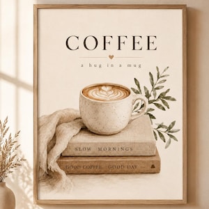 Pode incluir: Uma impressão de parede emoldurada com o texto COFFEE a hug in a mug acima de uma caneca de cerâmica salpicada com latte art, apoiada em dois livros empilhados rotulados SLOW MORNINGS e GOOD COFFEE GOOD DAY, com tecido bege e folhas verdes.