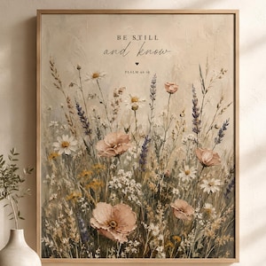 May include: A framed wall art print featuring a field of wildflowers in muted tones of beige, white, pink, and purple. The text "BE STILL and know" and "PSALM 46:10" is printed in black at the top centre above the floral illustration.