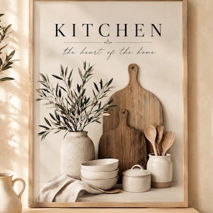 Op de afbeelding: Een ingelijste wandprint met de tekst KITCHEN the heart of the home. De afbeelding toont een lichte keramische vaas met olijftakken, een stapel van drie kommen, een pot met deksel, houten snijplanken en houten keukengerei.