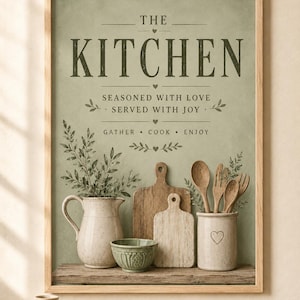 Op de afbeelding: Een ingelijste wandprint met een saliegroene achtergrond en de tekst THE KITCHEN, SEASONED WITH LOVE, SERVED WITH JOY, GATHER, COOK, ENJOY. Het toont een kan, een kleine groene kom, twee houten snijplanken en een houder voor keukengerei.