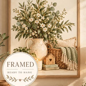 May include: A framed wall art print featuring a bouquet of white flowers and green foliage in a speckled ceramic pitcher. Beside it sits a woven basket with a green tasseled throw, a small wooden house, and a lit candle. Text reads FRAMED READY TO HANG.