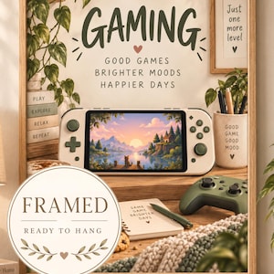 Puede incluir: Un cuadro enmarcado que muestra una consola de juegos portátil con un paisaje al atardecer, rodeado de textos como GAMING, GOOD GAMES BRIGHTER MOODS HAPPIER DAYS y JUST ONE MORE LEVEL, con un sello circular FRAMED READY TO HANG.