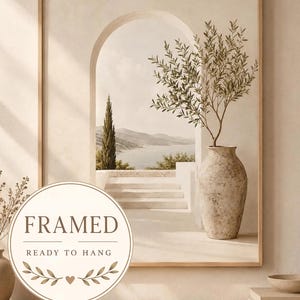 Könnte beinhalten: Ein gerahmter Kunstdruck mit einer mediterranen Landschaft, einem Torbogen, Steinstufen, einem entfernten Meer und einer hohen Zypresse. Eine strukturierte beige Vase mit einem Olivenzweig steht im Vordergrund. Der Text lautet FRAMED READY TO HANG.