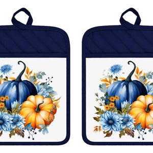 May include: A pair of rectangular oven mitts with dark navy blue quilted fabric borders and hanging loops. The center features a white panel printed with a vibrant illustration of a large dark blue pumpkin, an orange pumpkin, and blue flowers.