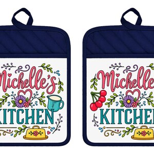 May include: Two rectangular navy blue pot holders with a white center panel featuring the text Michelle's KITCHEN in pink and teal. The design includes illustrations of red cherries, a purple flower, a teal pitcher, and a yellow butter dish.