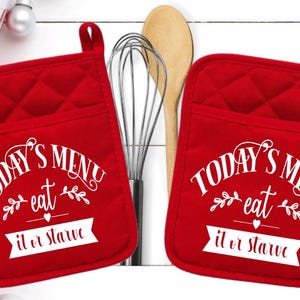 May include: Two square red quilted pot holders featuring white text that reads Today's Menu eat it or starve with decorative leaf and heart accents. Each pot holder includes a small fabric loop at the top corner for convenient hanging storage.