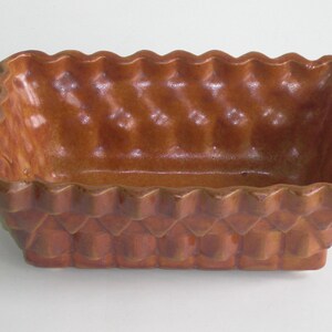 May include: A brown ceramic baking dish with a woven basket design. The dish has a rectangular shape with a wavy edge.