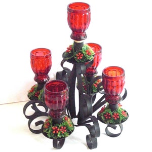 May include: A black metal candelabra with five red glass candle holders. Each holder is decorated with a small green and red garland.