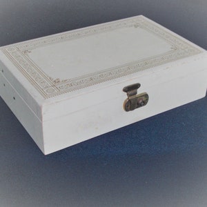 May include: A white wooden box with a gold decorative border and a brass latch. The box has a plain white interior.