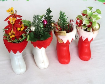 May include: Four miniature Christmas boot ornaments. Each boot is red and white, with a decorative arrangement of artificial plants and ornaments inside. The boots are arranged in a row, perfect for holiday decor.