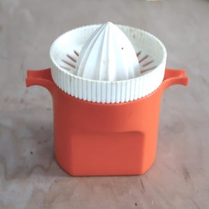 May include: Orange and white citrus juicer. The juicer has a white reamer and strainer set inside an orange container with two handles. The juicer is designed for squeezing citrus fruits.