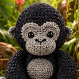 Puede incluir: Un peluche de gorila tejido a ganchillo con hilo gris oscuro en el cuerpo y la cabeza, con detalles en hilo gris claro en la cara y el vientre. El juguete tiene grandes ojos redondos de plástico negro y pequeñas orejas redondeadas.
