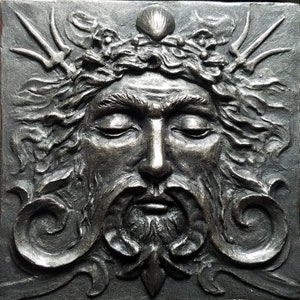 May include: A detailed, silver-toned, sculpted relief of a man's face with a crown of seaweed and a seashell on top. The man's eyes are closed and he has a long beard and mustache.