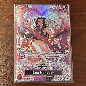 May include: A trading card featuring Boa Hancock from the Seven Warlords of the Sea/Kuja Pirates. The card has a holographic background with a heart-shaped design. The card has the number 2 and the text "3000 特" in the upper corners. The card also has text describing the card's abilities.