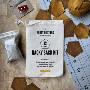 May include: A "Footy Footbag Hacky Sack Kit" with a canvas bag, microsuede panels, sewing supplies, and sand filling. The kit includes 12 precut panels, a sewing clip, thread, a needle, and 60g of sand. The bag has the text "Footy Footbag" and "Hacky Sack Kit".