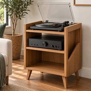 May include: A light brown wooden media console with three open shelves. The top shelf holds a black record player with a clear dust cover. The middle shelf contains a black audio amplifier with a central volume knob and several smaller dials.