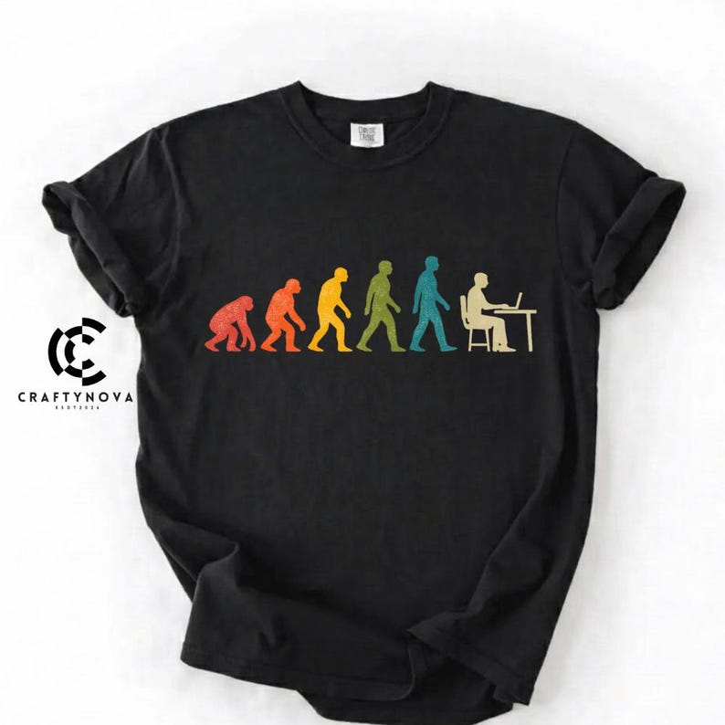 Peut inclure: Un t-shirt noir &agrave; manches courtes arborant un graphique color&eacute; de l'&eacute;volution humaine, allant d'un primate &agrave; une personne assise &agrave; un bureau avec un ordinateur portable. Le motif inclut le texte CRAFTYNOVA sur le c&ocirc;t&eacute; gauche du tissu.